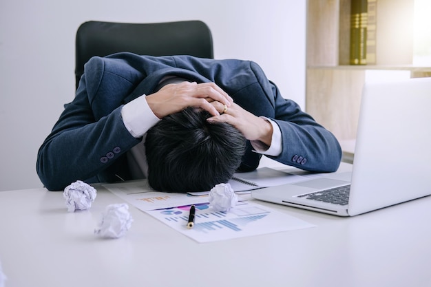 Un homme d'affaires stressé reposant la tête sur son bureau au bureau.