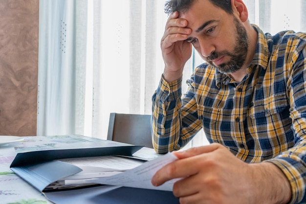 Un homme d'affaires stressé avec la tête dans les mains lisant un document sur son bureau.