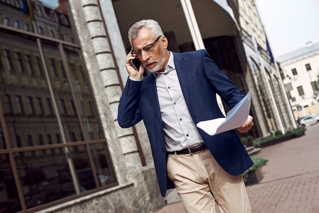 Un homme d'affaires supérieur discute au téléphone d'un contrat à l'extérieur près du bureau