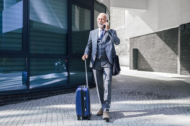 Homme d'affaires supérieur avec la valise parlant au téléphone intelligent