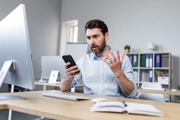 Homme d'affaires surpris et choqué dans le bureau, l'homme regarde l'écran du téléphone et lit les nouvelles en ligne