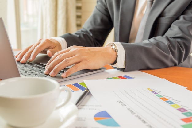 Homme d'affaires en tapant un ordinateur portable et travailler sur le rapport financier sur table.