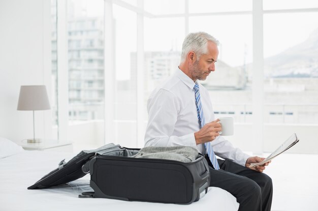 Homme d&#39;affaires avec une tasse de café en lisant le journal par les bagages à la chambre d&#39;hôtel