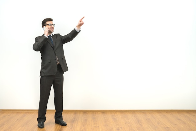 L'homme d'affaires téléphone et fait des gestes sur le fond du mur blanc