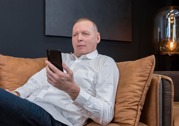 Homme d'affaires avec un téléphone portable sur un canapé homme utilisant un message de lecture de textos smartphione