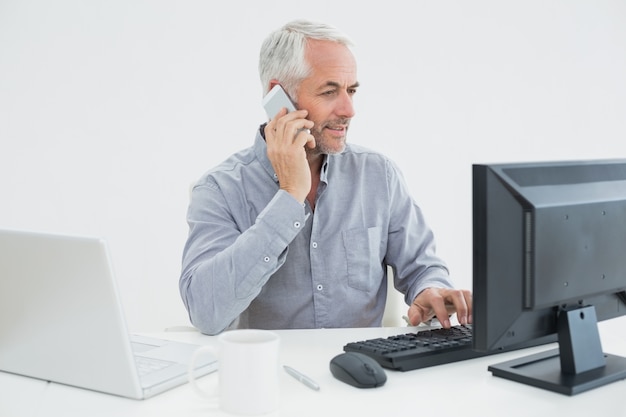 Homme d&#39;affaires avec téléphone portable, ordinateur portable et ordinateur au bureau