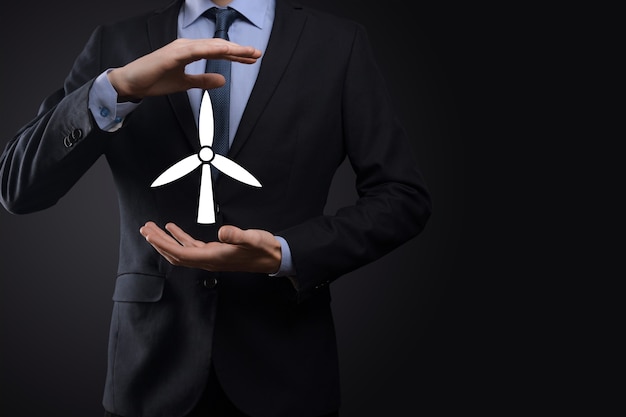 Homme d'affaires tenant une icône d'un moulin à vent qui produit de l'énergie environnementale. Fond sombre