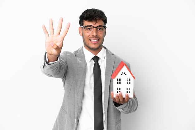 Homme d'affaires tenant une maison isolée sur fond bleu heureux et comptant quatre avec les doigts