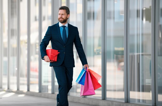 Homme d'affaires tenant des sacs d'achat et marchant dans le magasin d'achat achetant et payant shopaholic