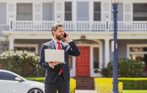 Homme d'affaires tenant son ordinateur portable tout en utilisant son téléphone et debout dans la rue