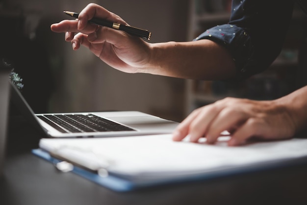 Homme d'affaires tenant un stylo et de la paperasse avec un ordinateur portable sur le bureau