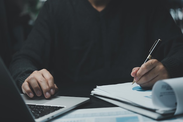 Homme d'affaires tenant un stylo pointant vers le plan graphique de marketing, l'investissement financier et la stratégie commerciale, le tableau de données, le rapport et le travail sur l'ordinateur portable au bureau