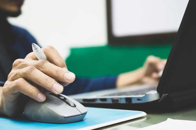 Homme d'affaires tenant un stylo et en utilisant le contrôle de la souris sur un ordinateur portable au travail