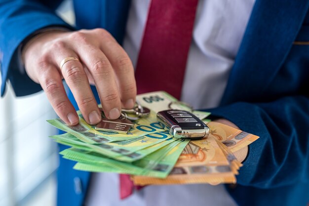 L'homme d'affaires tient la clé de la voiture et de la maison avec de l'argent en euros. investissement pour l'avenir