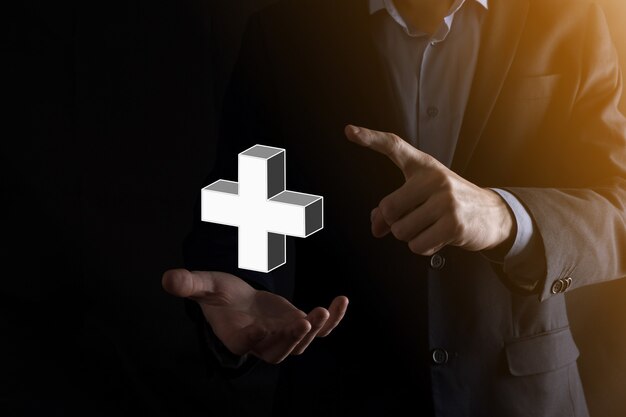 L'homme d'affaires tient l'icône 3D plus, l'homme tient dans la main une offre positive telle que le profit, les avantages, le développement, la RSE représentée par le signe plus. La main montre le signe plus.