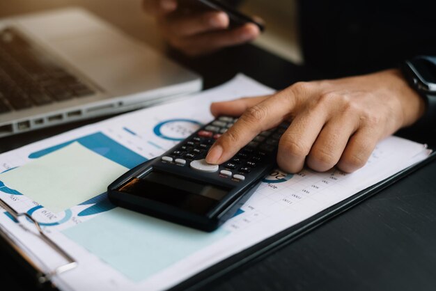 Homme d'affaires travaillant sur un bureau à l'aide d'une calculatrice et d'un smartphone pour calculer le concept de comptabilité financière des nombres