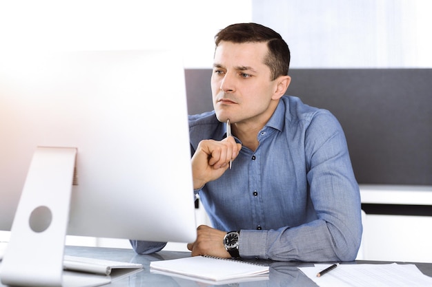 Homme d'affaires travaillant avec un ordinateur dans un bureau moderne et ensoleillé. Tête d'un entrepreneur masculin ou d'un directeur d'entreprise sur le lieu de travail. Notion d'entreprise.