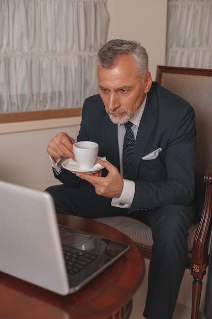 Homme d'affaires travaillant sur un ordinateur portable et buvant du café assis dans le hall de l'hôtel et attendant l'enregistrement