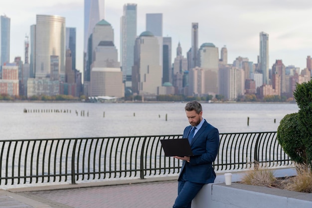 Homme d'affaires travaillant sur un ordinateur portable en plein air Homme daffaires tapant sur un appareil portable à New York Homme d‘affaires travaillant en ligne Homme d ́affaires prospère travaillant en freelance en ligne Succès en affaires Espace de copie
