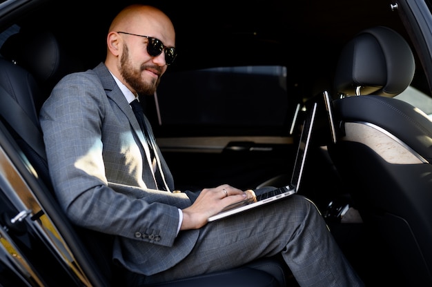 Homme d'affaires travaillant sur ordinateur portable sur le siège arrière de la voiture exécutive. Concept d'affaires, succès, voyages, luxe.