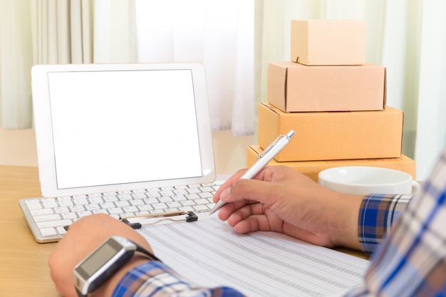 Homme d'affaires travaillant avec un téléphone portable et l'emballage de la boîte de colis brune à la maison. le vendeur de mains prépare le produit prêt à livrer au client. Vente en ligne, commerce électronique Démarrage du concept d'expédition.