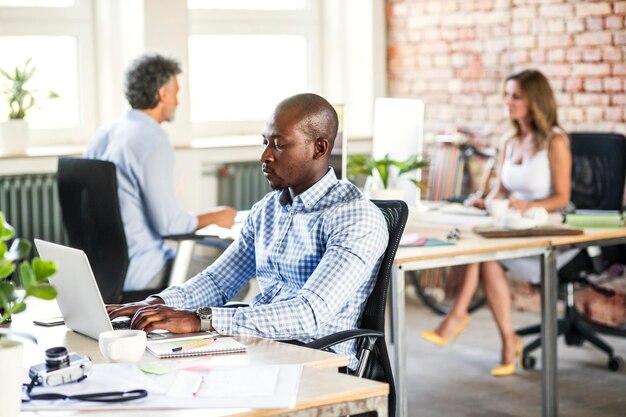 Homme d'affaires utilisant un ordinateur portable au bureau au bureau avec des collègues en arrière-plan