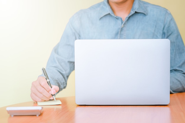 Photo un homme d'affaires utilisant un ordinateur portable pour rechercher des informations et prendre des notes sur papier.