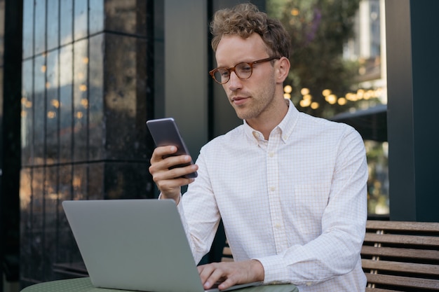 Homme d'affaires utilisant un ordinateur portable tenant un téléphone portable regardant un écran numérique Indépendant travaillant en ligne