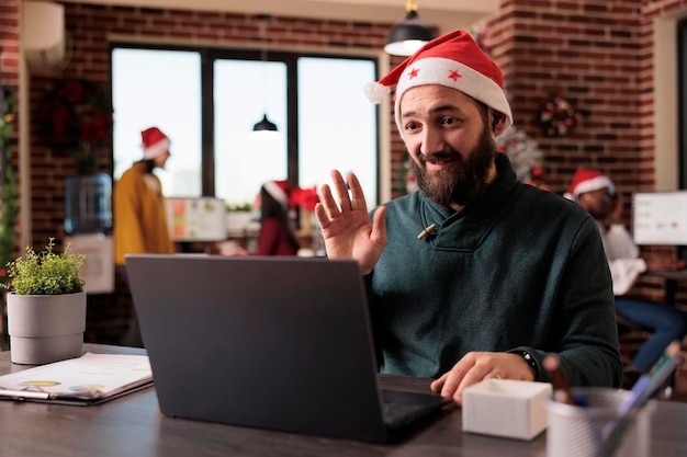 Homme d'affaires utilisant une réunion d'appel vidéo en ligne au travail, assis dans un bureau décoré d'ornements de noël et d'arbre. Personne parlant sur le chat de vidéoconférence à distance, discussion par téléconférence.