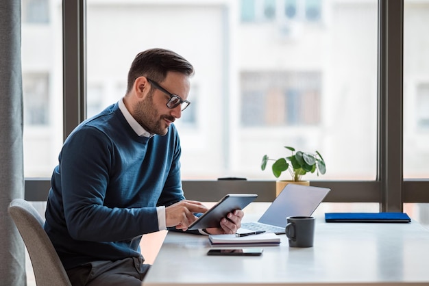 Homme d'affaires utilisant une tablette numérique tout en travaillant sur un ordinateur portable au bureau