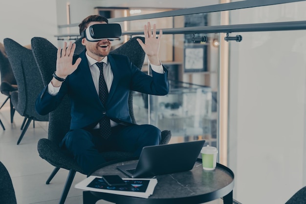 Homme d'affaires vêtu d'un costume formel portant des lunettes vr tout en travaillant sur un ordinateur portable au café