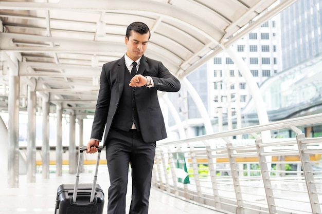 Homme d'affaires vêtu d'un costume avec une valise transportant un bagage, il avait un air inquiet sur son visage, il marchait à la hâte et regardait sa montre alors qu'il marchait - concept de gens d'affaires de style de vie