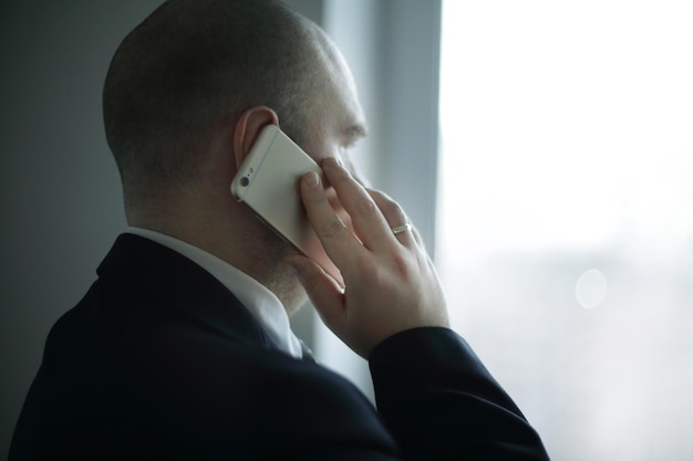 Homme d'affaires de vue arrière avec smartphone regardant par la fenêtre du bureau