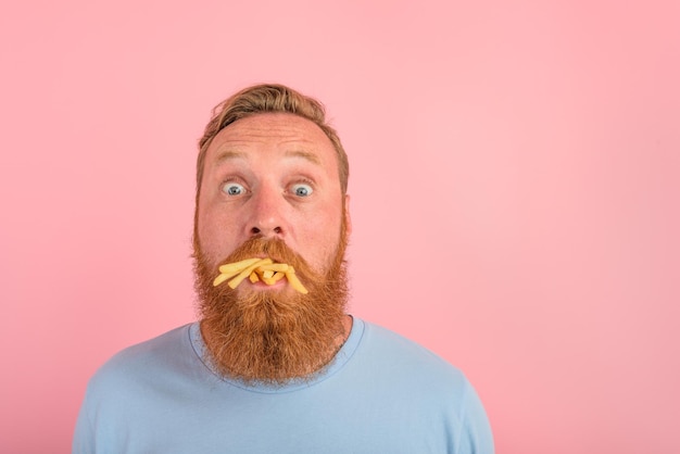 Photo un homme affamé avec de la barbe et des tatouages mange un sandwitch avec un hamburger et des pommes de terre