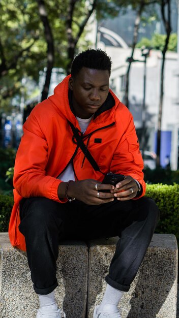 Homme africain assis sur un banc envoyant des SMS avec son téléphone dans ses mains.
