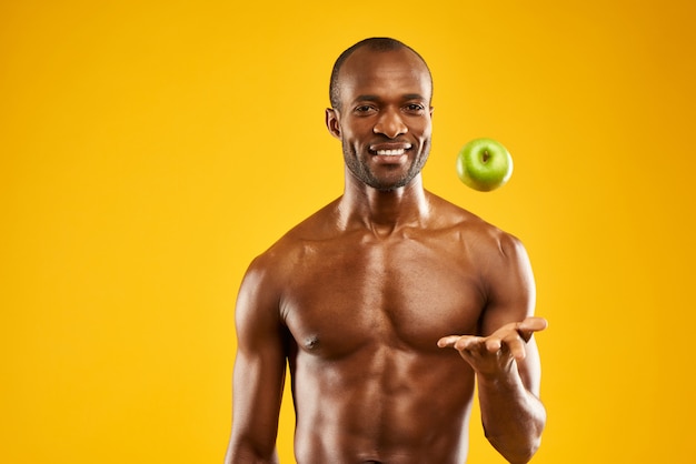 Un homme africain au torse nu jette une pomme en l&#39;air.