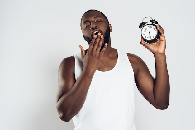 Homme africain bâille tenant un réveil.