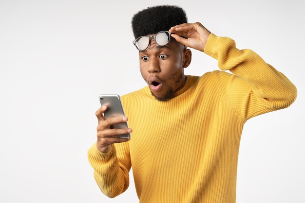 Homme africain choqué tout en regardant dans un smartphone sur fond blanc isolé