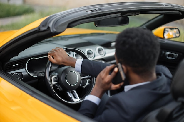 Homme africain en costume d'affaires utilisant et parlant sur un smartphone tout en conduisant une voiture