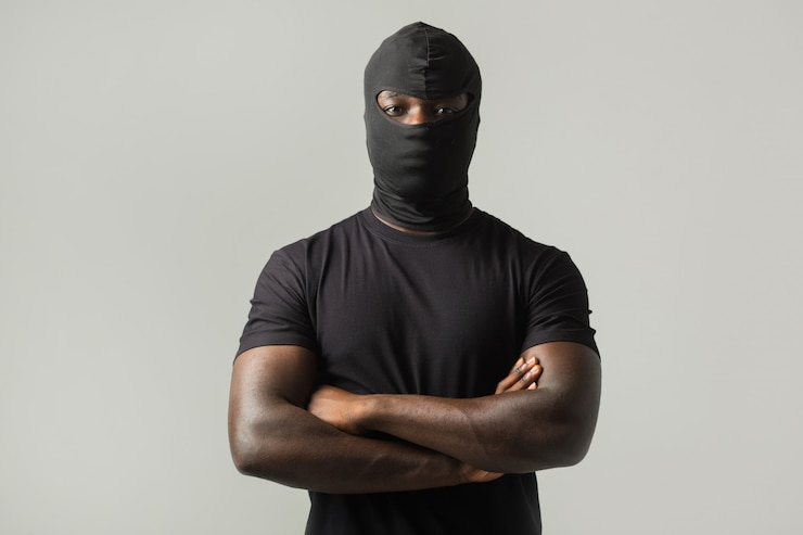 Photo homme africain dans un masque noir et un t-shirt noir sur un mur gris