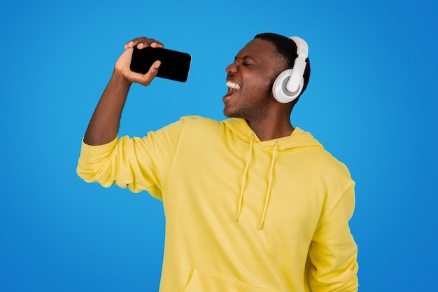 Un homme africain dans un sweat-shirt jaune chante joyeusement dans un smartphone comme un microphone