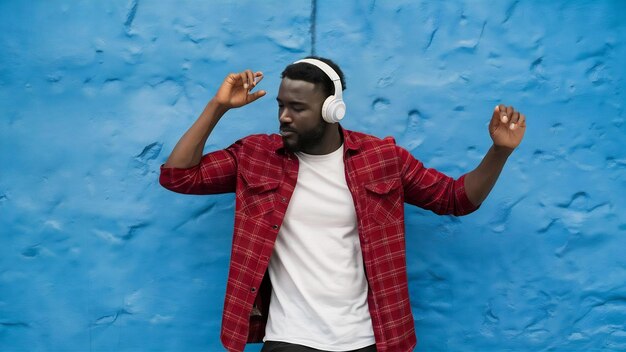 Photo un homme africain écoutant de la musique dans des écouteurs dansant sur un mur bleu