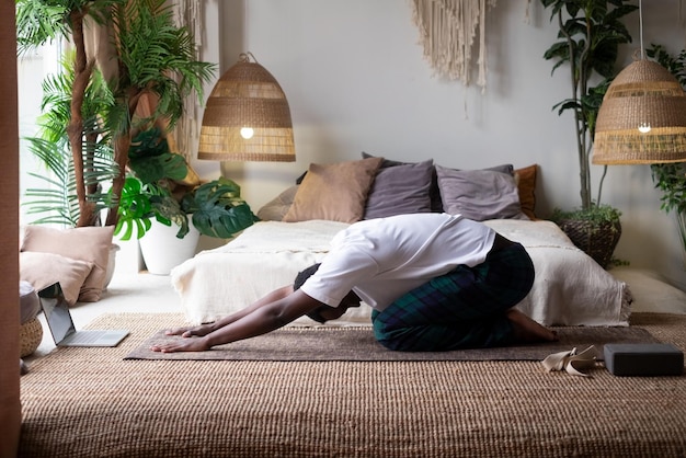 Homme africain faisant du yoga à la maison après une leçon de yoga se reposant à balasana