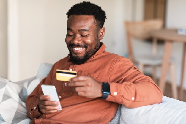 Un homme africain fait ses courses en ligne à l'aide d'un téléphone portable et d'une carte de crédit à l'intérieur