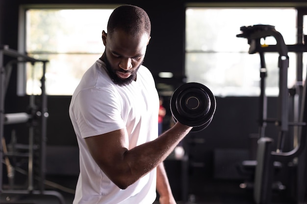 Homme africain en forme et musclé faisant des exercices de biceps avec des haltères dans l'espace de copie de la salle de gym