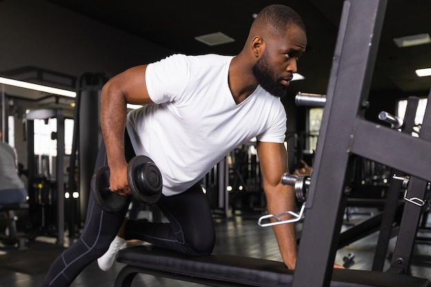 Un homme africain en forme et musclé s'entraîne avec des haltères