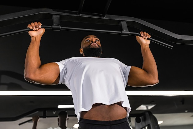 Homme africain en forme et musclé tirant sur la barre horizontale dans une salle de sport