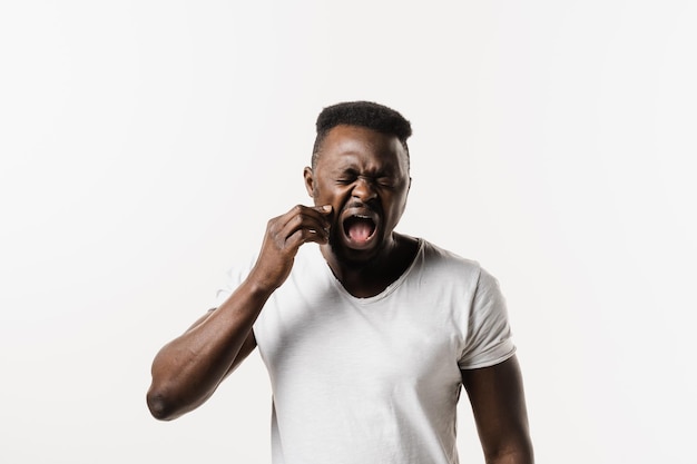 Homme africain avec une infection par la carie dentaire ou une blessure à la dent ou aux gencives sur fond blanc Un homme afro-américain touche la joue et ressent une douleur dentaire et un inconfort de la dent