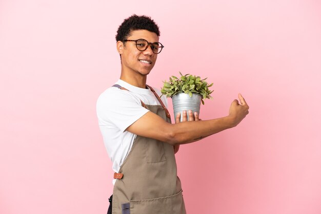 Homme africain de jardinier tenant une plante isolée sur fond rose pointant vers l'arrière