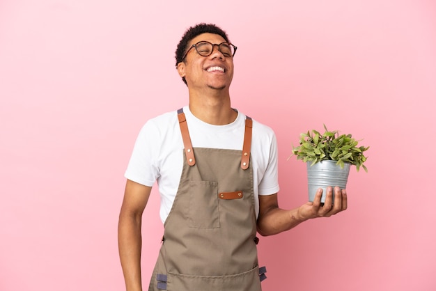 Homme africain de jardinier tenant une plante isolée sur fond rose en riant